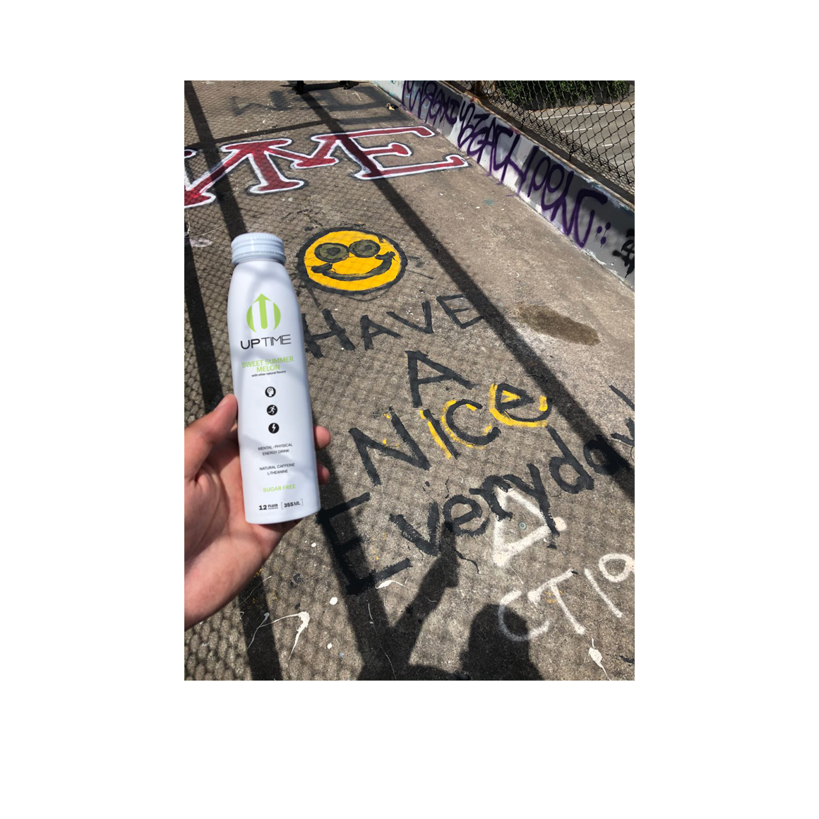 hand holding a can of uptime sweet summer melon energy drink over some sidewalk graffiti Image3