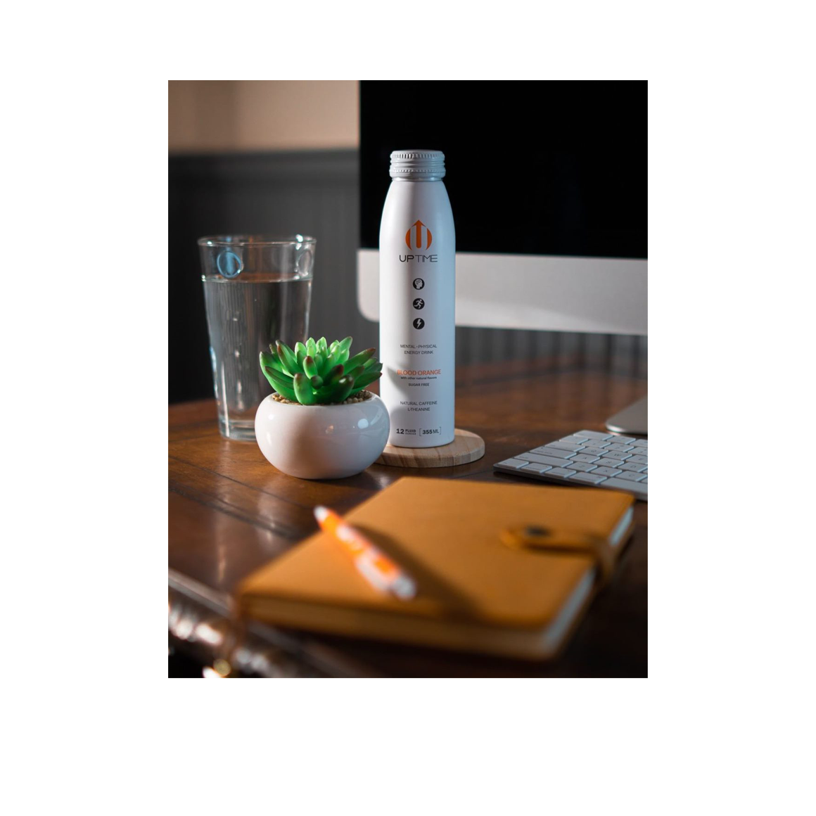 bottle of uptime blood orange energy drink on a desk with a plant Image4